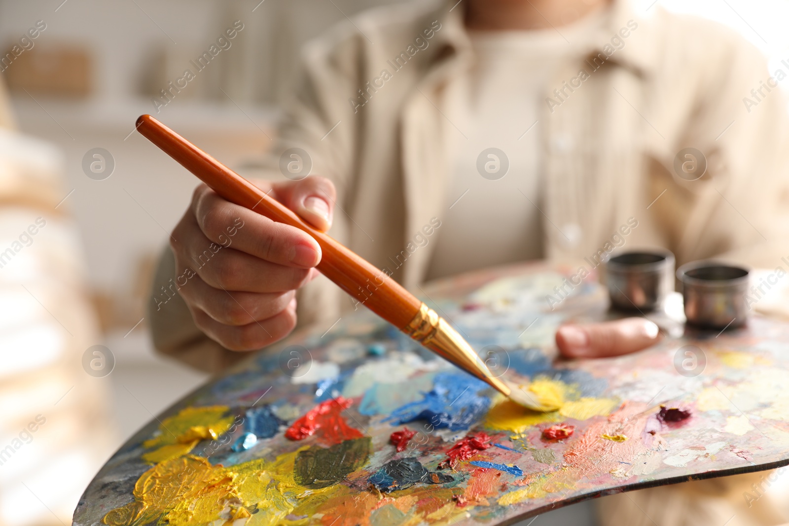 Photo of Woman mixing paints on palette with brush indoors, closeup