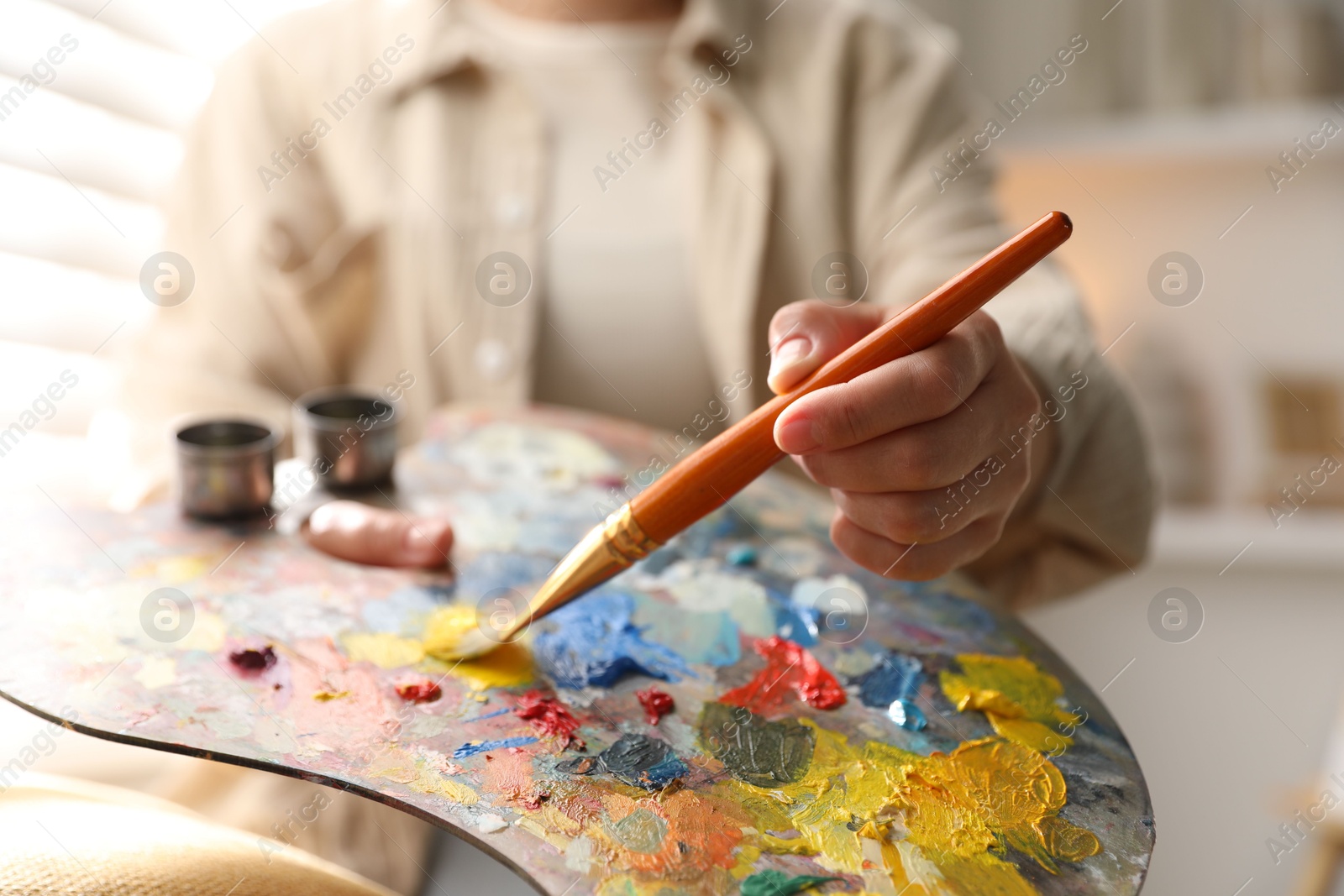 Photo of Woman mixing paints on palette with brush indoors, closeup