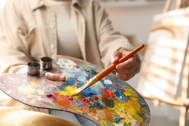 Photo of Woman mixing paints on palette with brush indoors, closeup