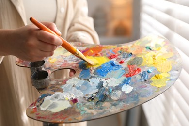 Photo of Woman mixing paints on palette with brush indoors, closeup