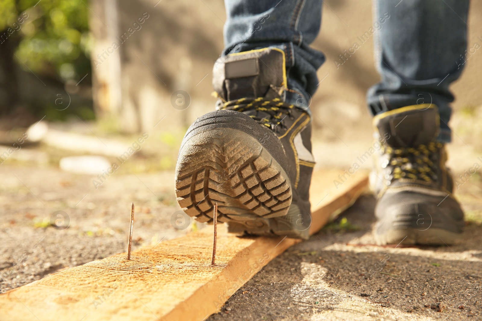 Photo of Careless worker stepping on nail in wooden plank outdoors, closeup