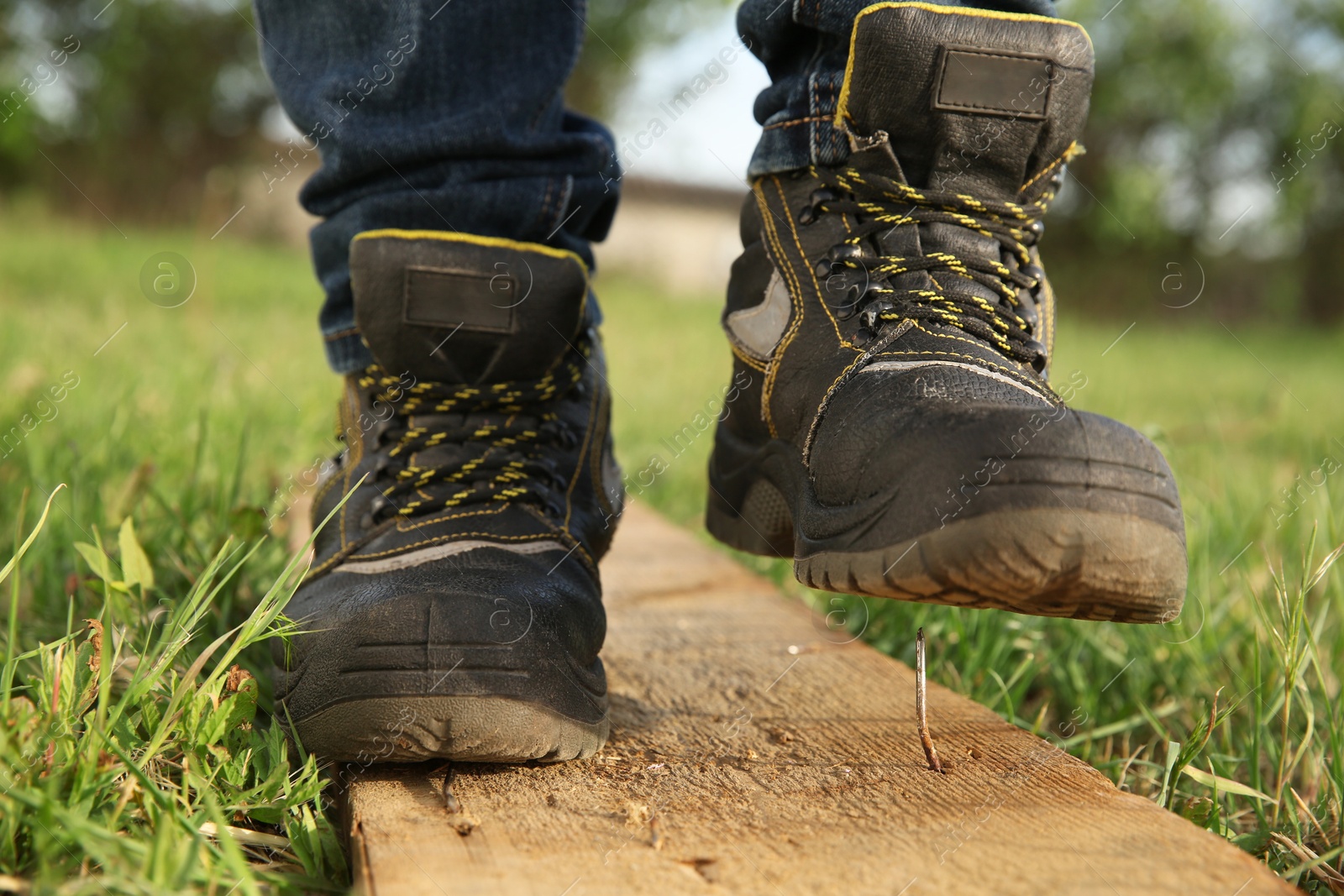 Photo of Careless worker stepping on nail in wooden plank outdoors, closeup