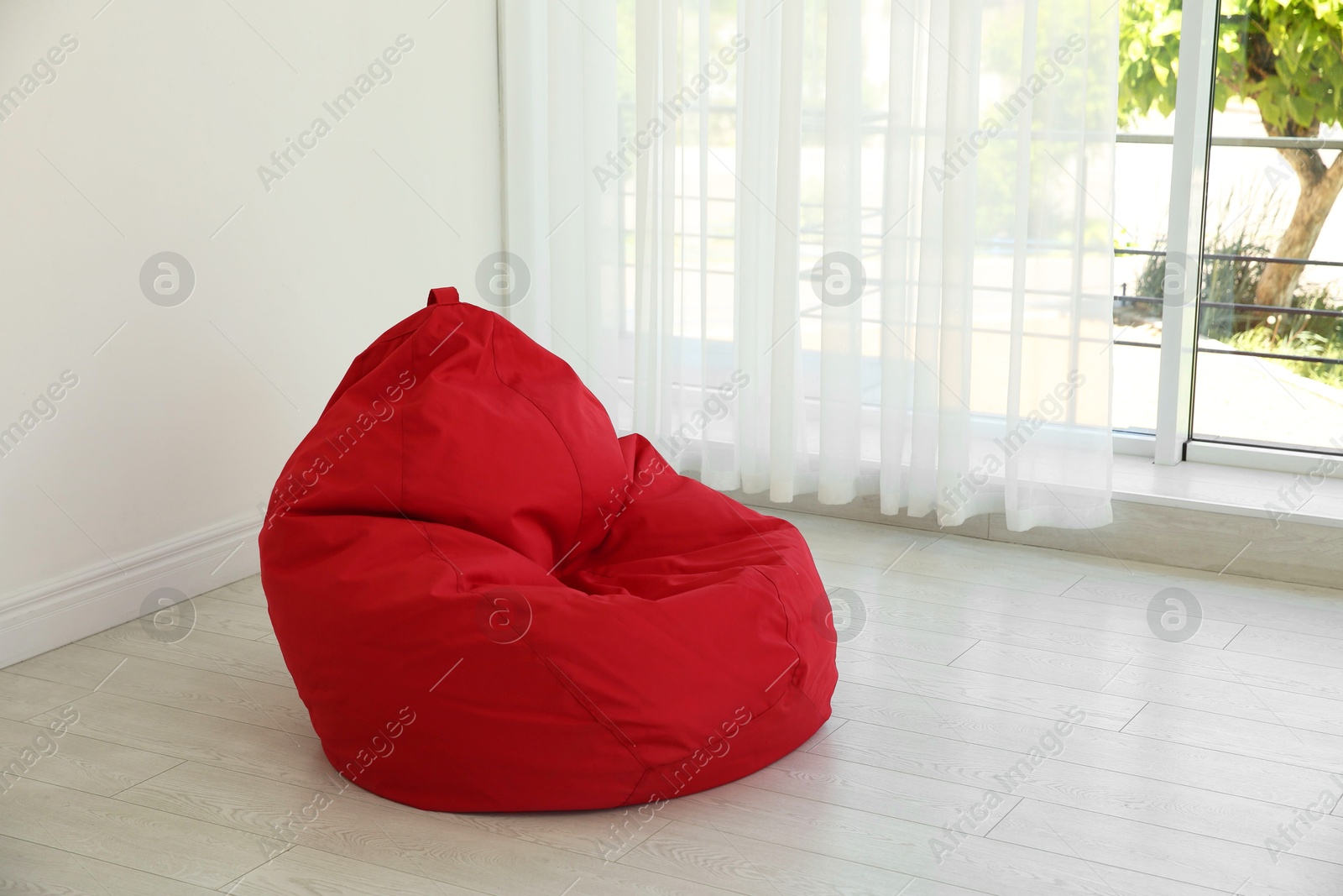 Photo of Red bean bag chair near window in room. Space for text