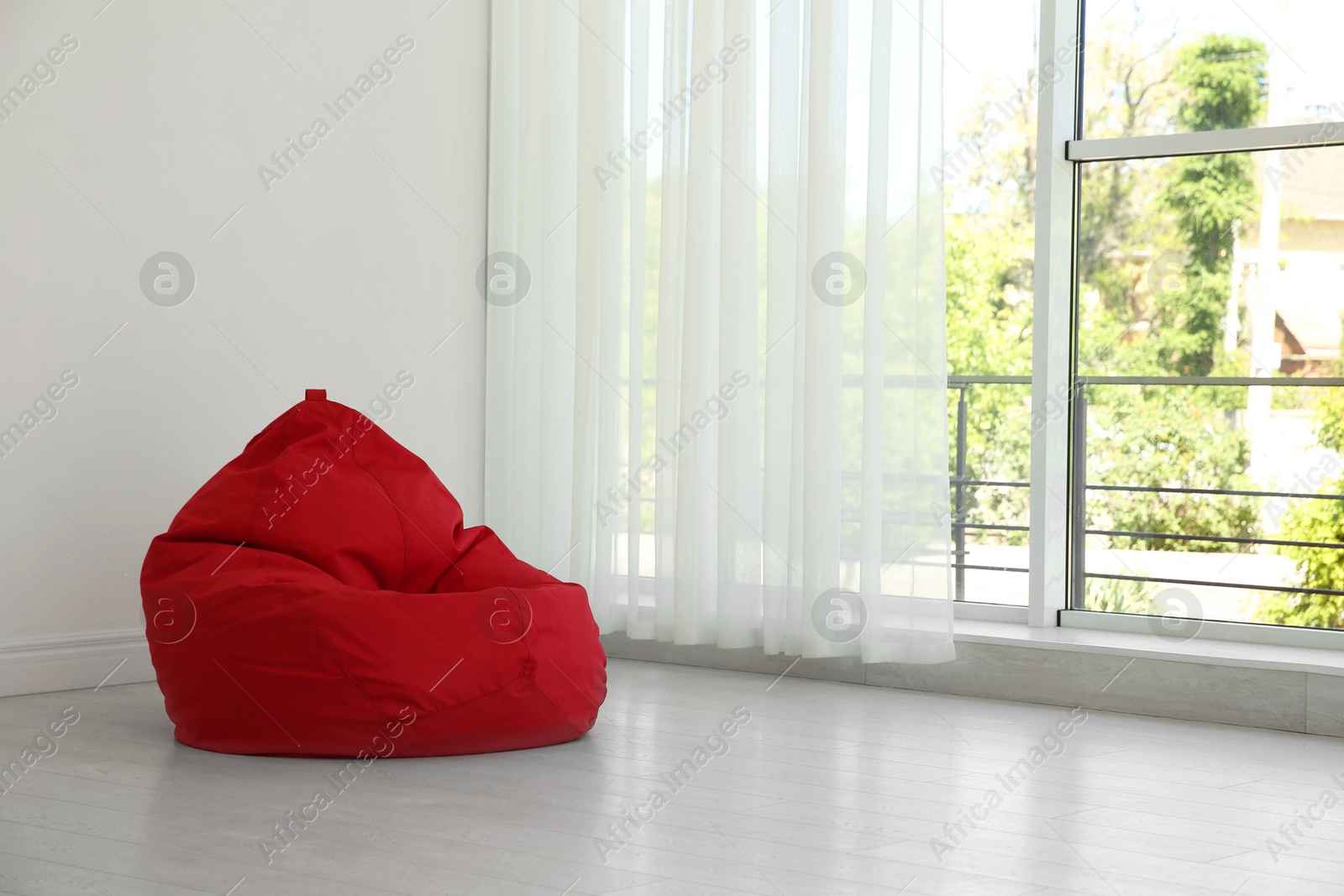 Photo of Red bean bag chair near window in room. Space for text