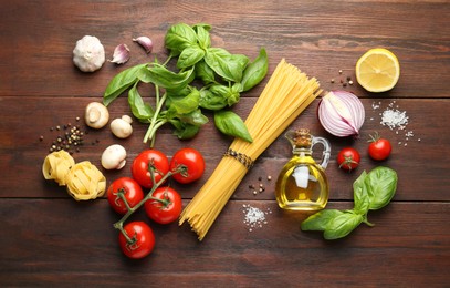 Photo of Different types of pasta, spices and products on wooden table, flat lay