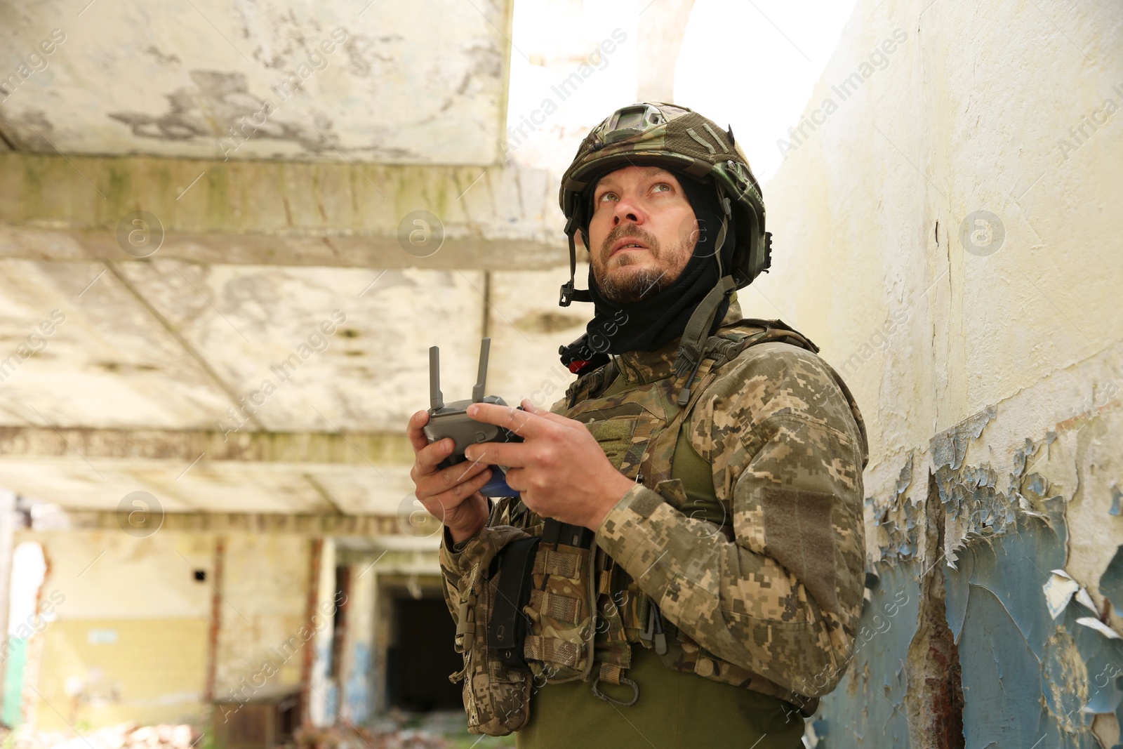 Photo of Military mission. Soldier in uniform with drone controller inside abandoned building, low angle view