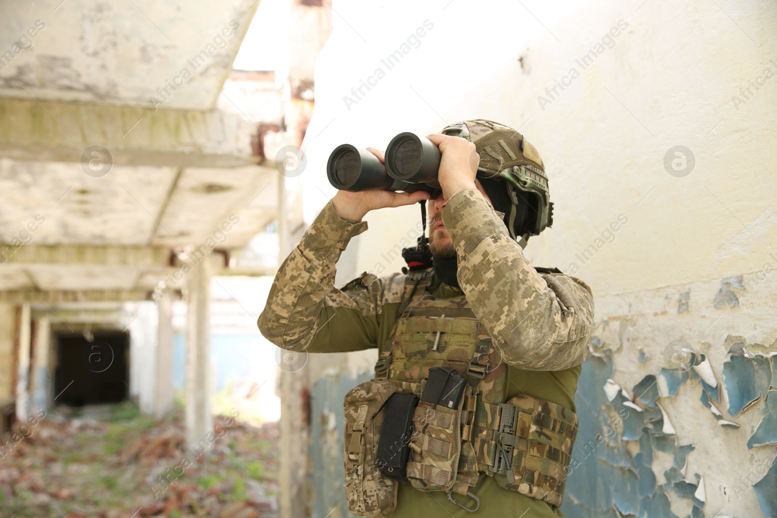 Photo of Military mission. Soldier in uniform with binoculars inside abandoned building