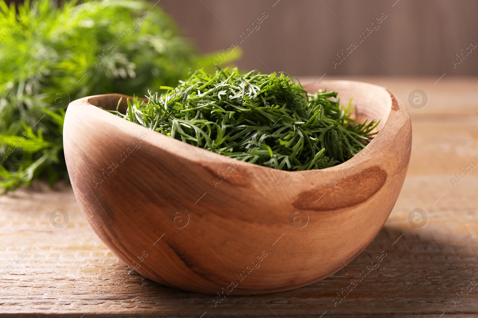 Photo of Fresh cut dill in bowl on wooden table, closeup