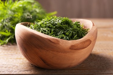 Photo of Fresh cut dill in bowl on wooden table, closeup