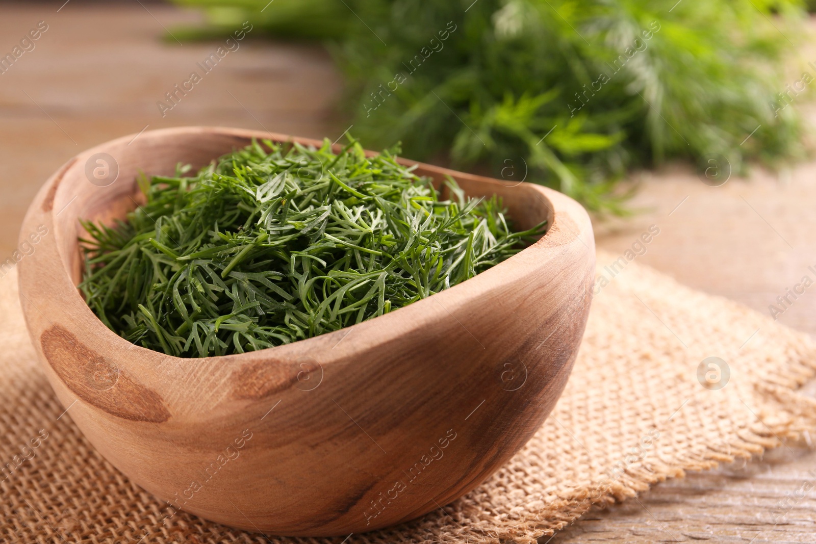 Photo of Fresh cut dill in bowl on wooden table, closeup