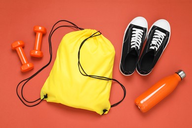 Photo of Yellow drawstring bag, thermo bottle, sneakers and dumbbells on crimson background, flat lay
