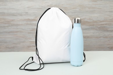 Photo of White drawstring bag and thermo bottle on light table