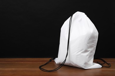 Photo of White drawstring bag on wooden table against black background. Space for text