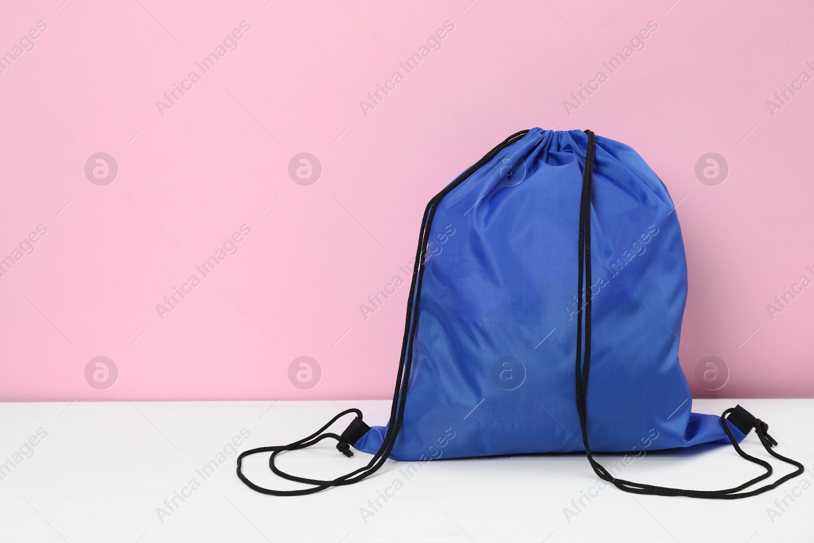 Photo of Blue drawstring bag on white wooden table against pink background. Space for text