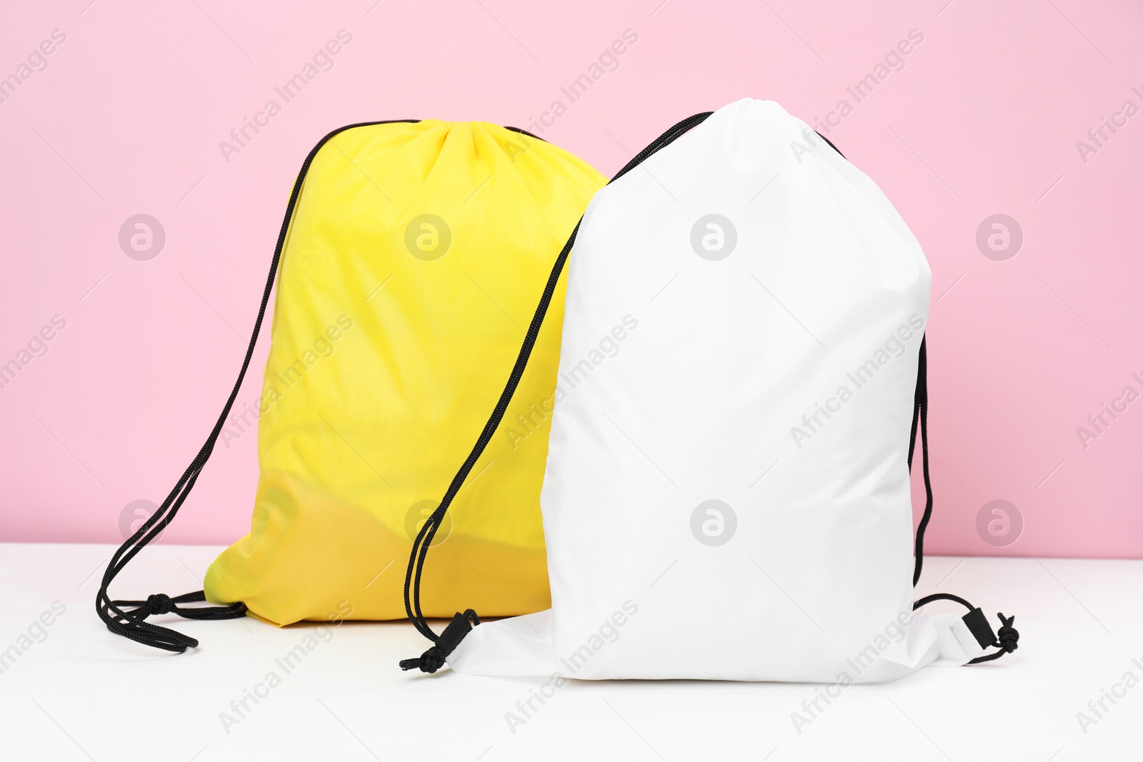 Photo of Two drawstring bags on white wooden table against pink background