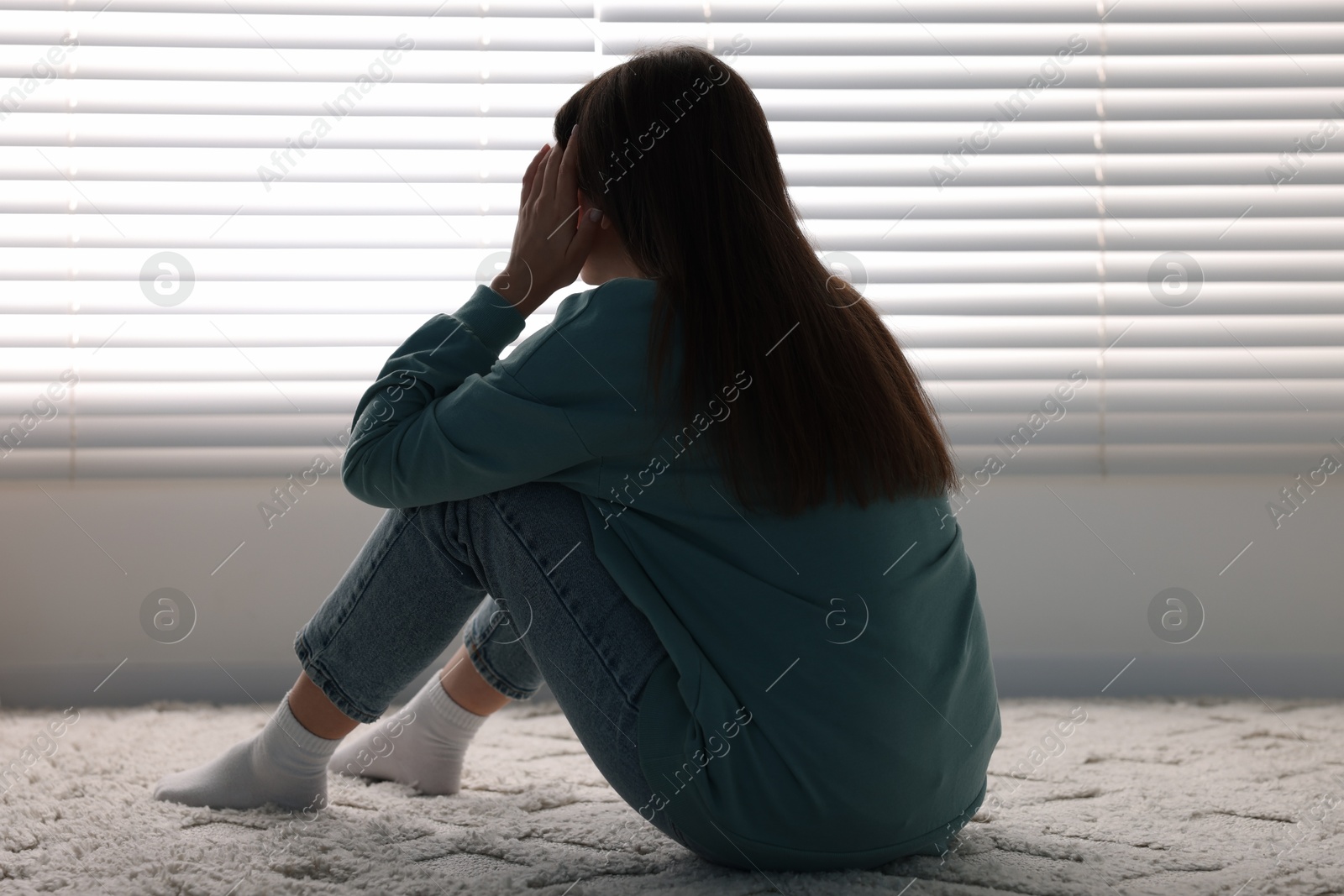 Photo of Loneliness concept. Sad woman sitting on floor at home, back view