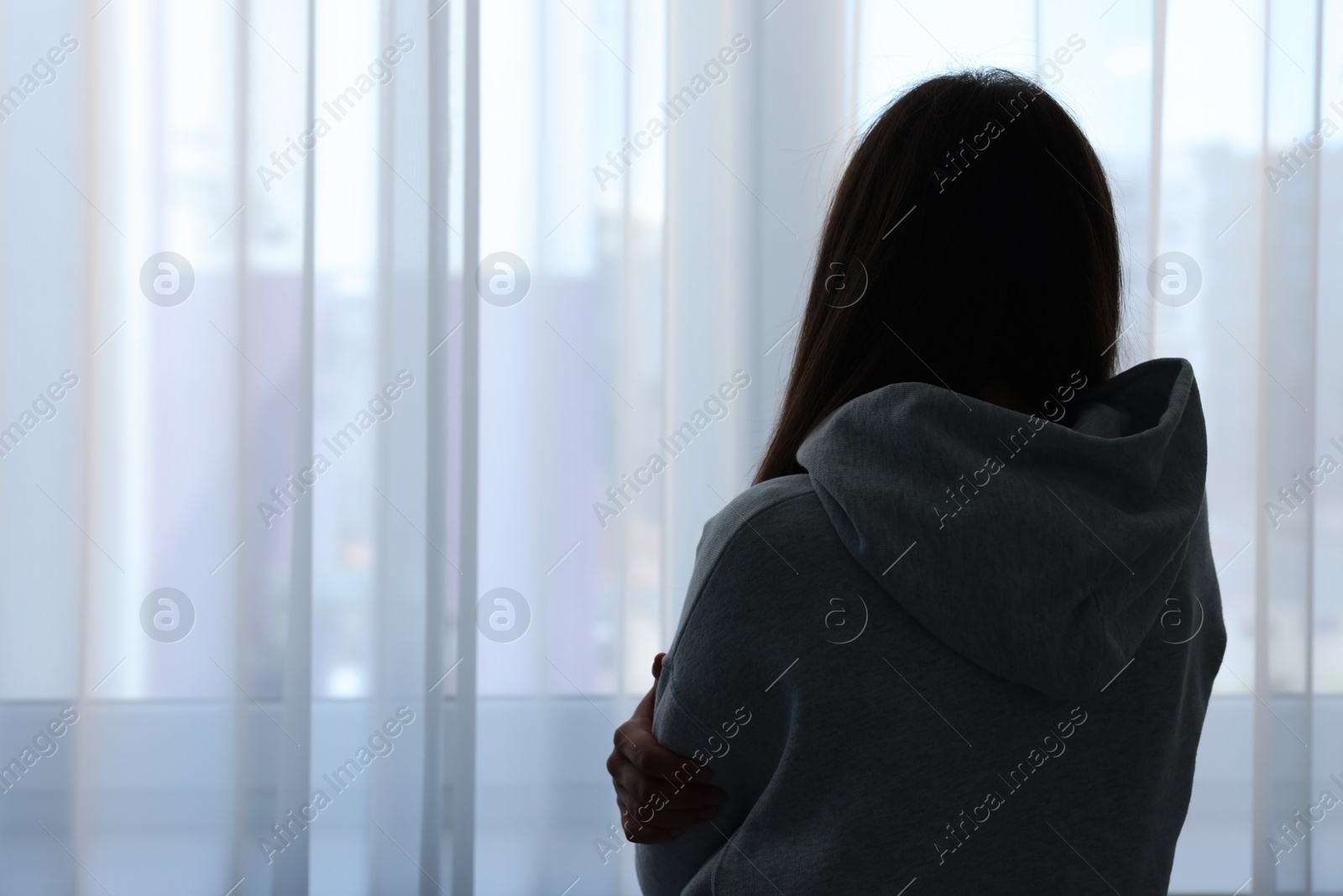 Photo of Loneliness concept. Sad woman near window at home, back view. Space for text