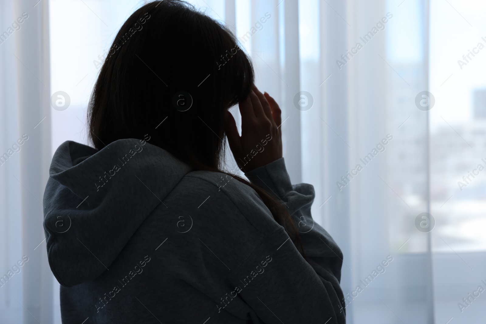 Photo of Loneliness concept. Sad woman near window at home, back view