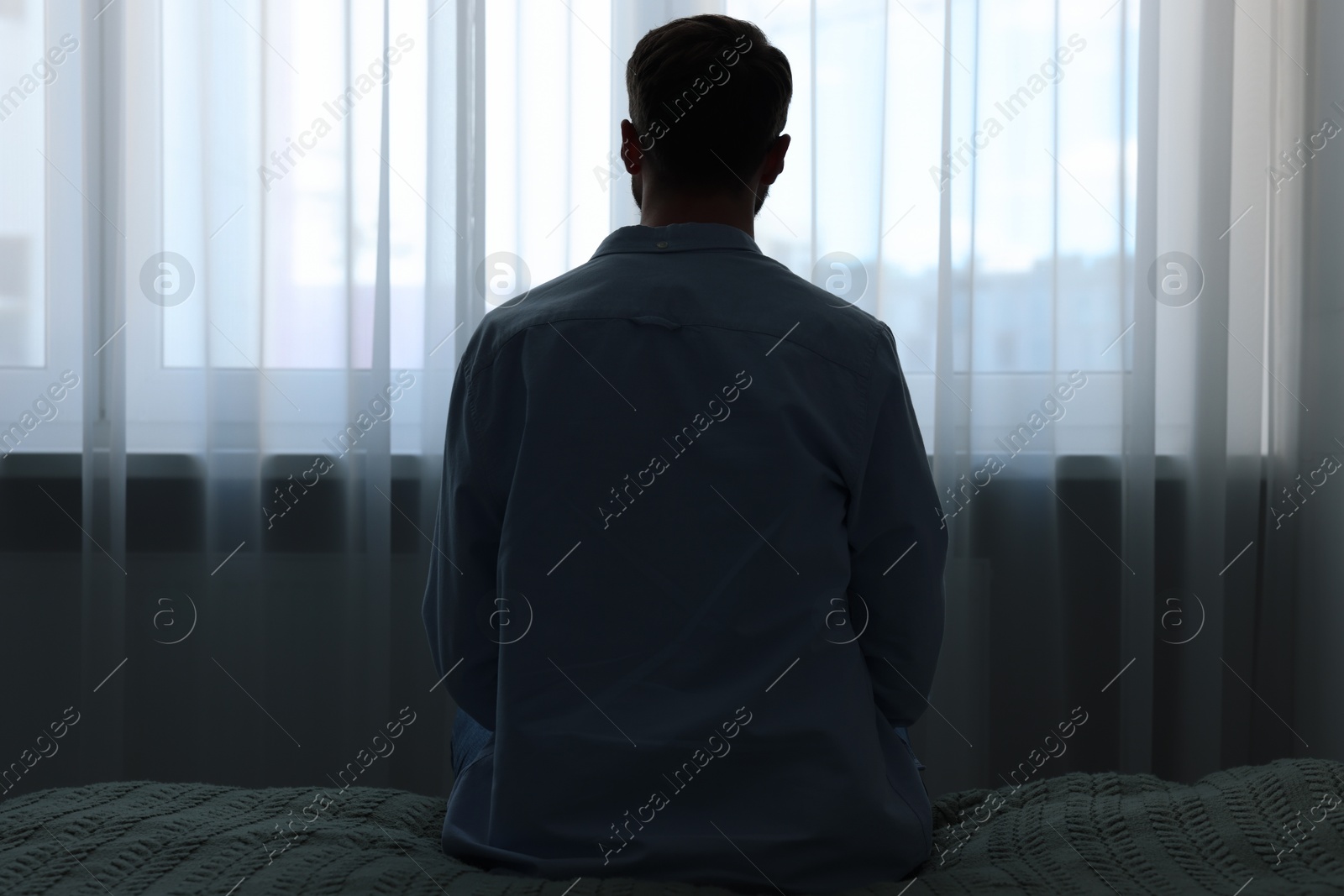 Photo of Loneliness concept. Sad man sitting on bed at home, back view