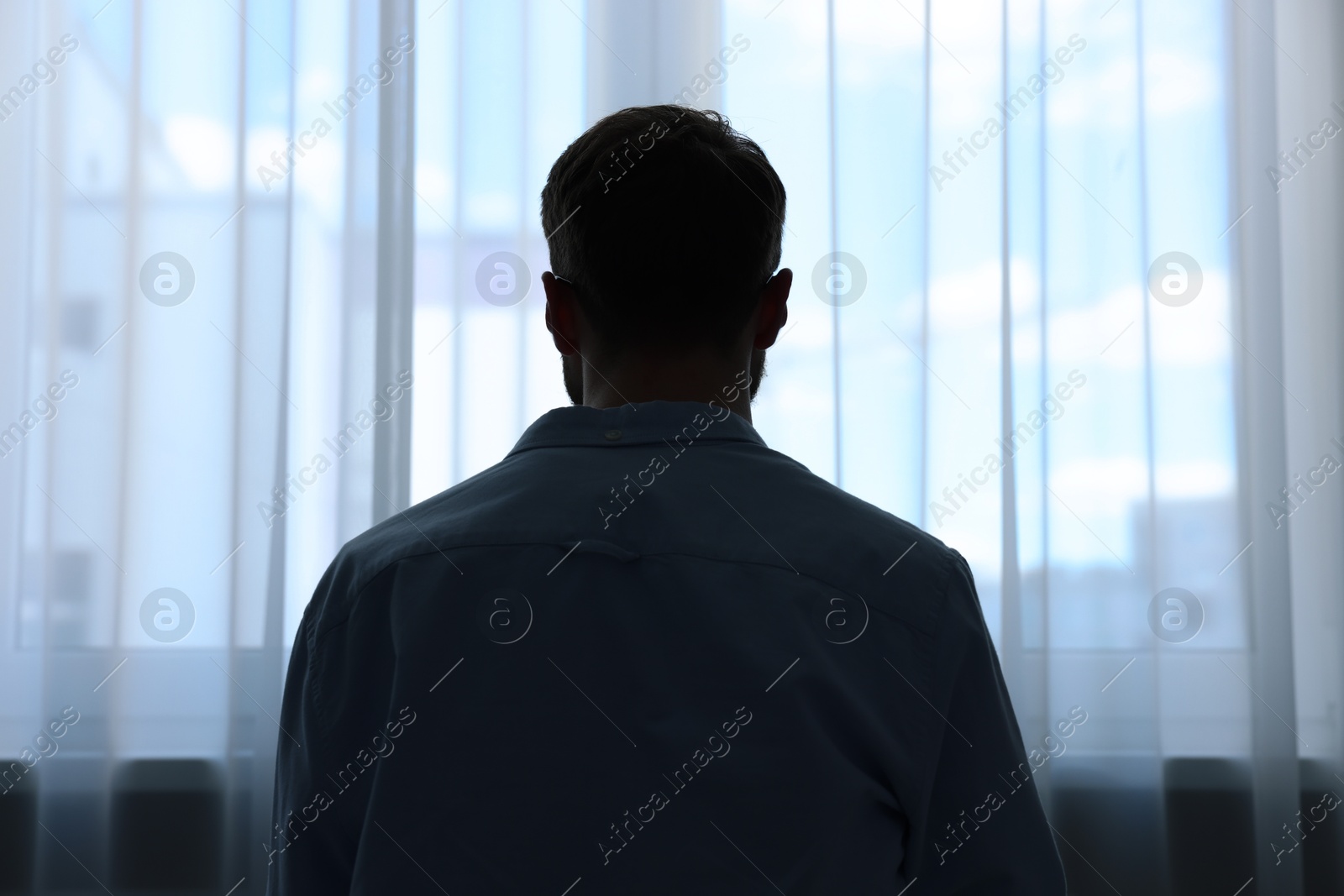 Photo of Loneliness concept. Sad man near window at home, back view