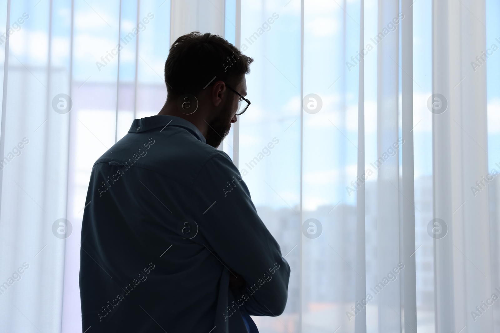 Photo of Loneliness concept. Sad man near window at home, back view. Space for text