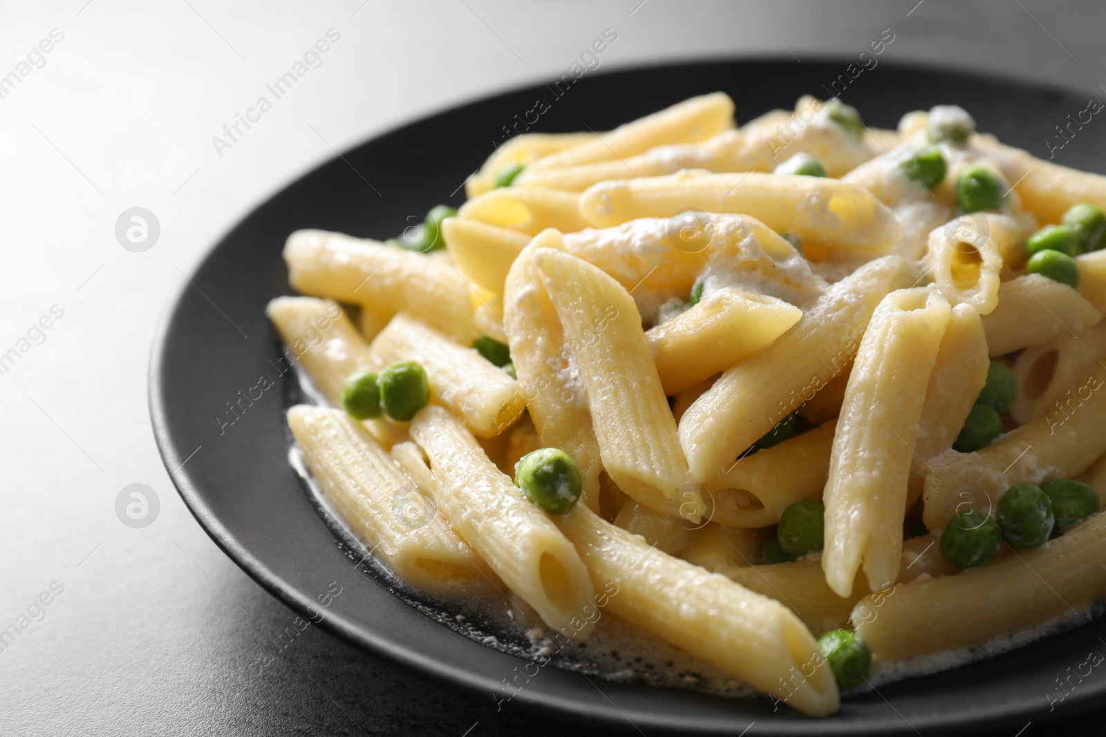 Photo of Delicious pasta with green peas and creamy sauce on grey table, closeup