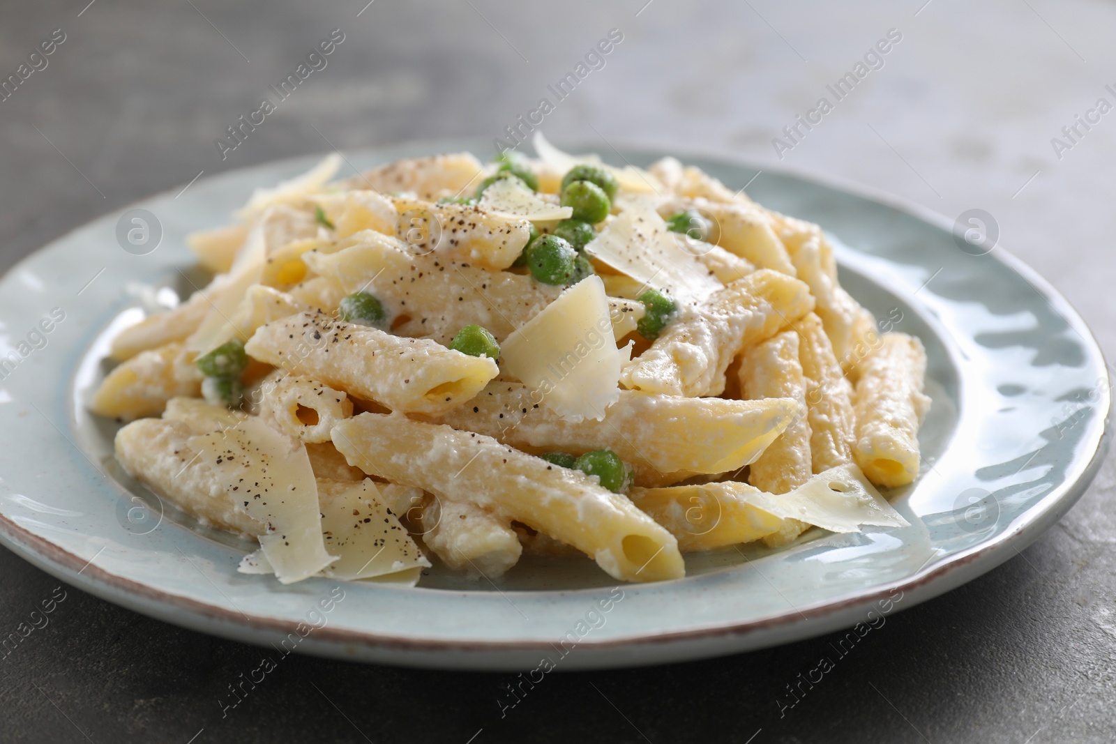 Photo of Delicious pasta with green peas, cheese and creamy sauce on grey table, closeup