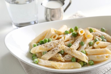 Photo of Delicious pasta with green peas and creamy sauce in bowl on white table, closeup