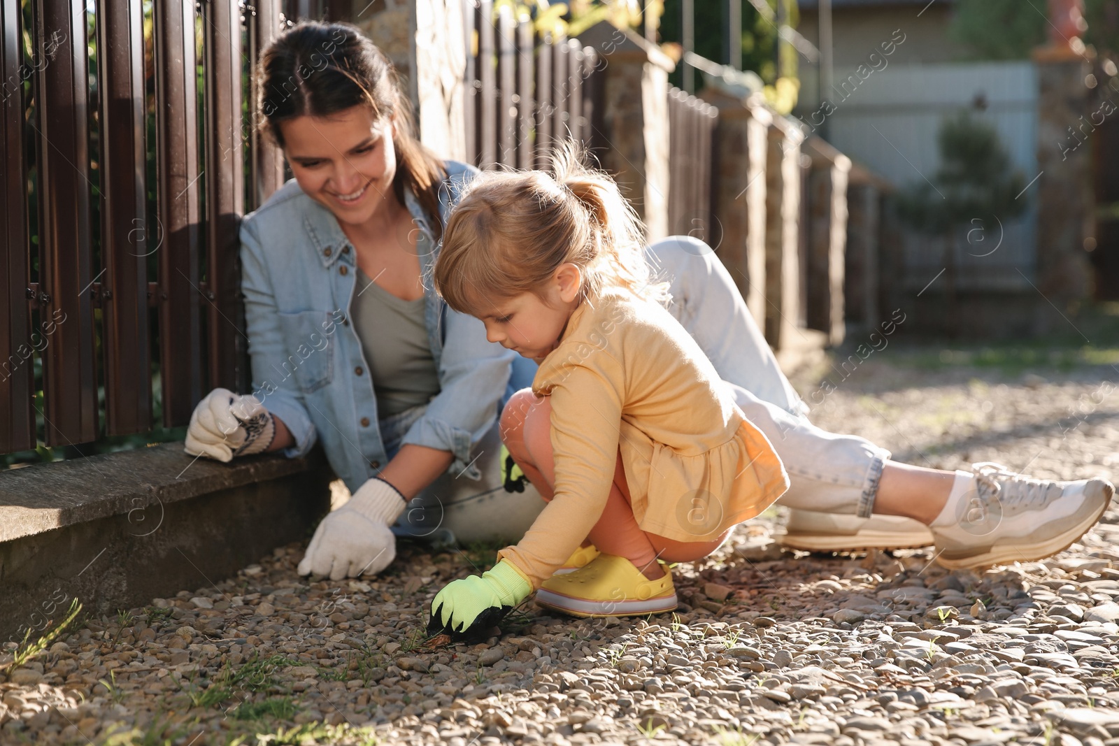 Photo of Mother and her cute daughter spending time together while pulling out grass near house on spring day