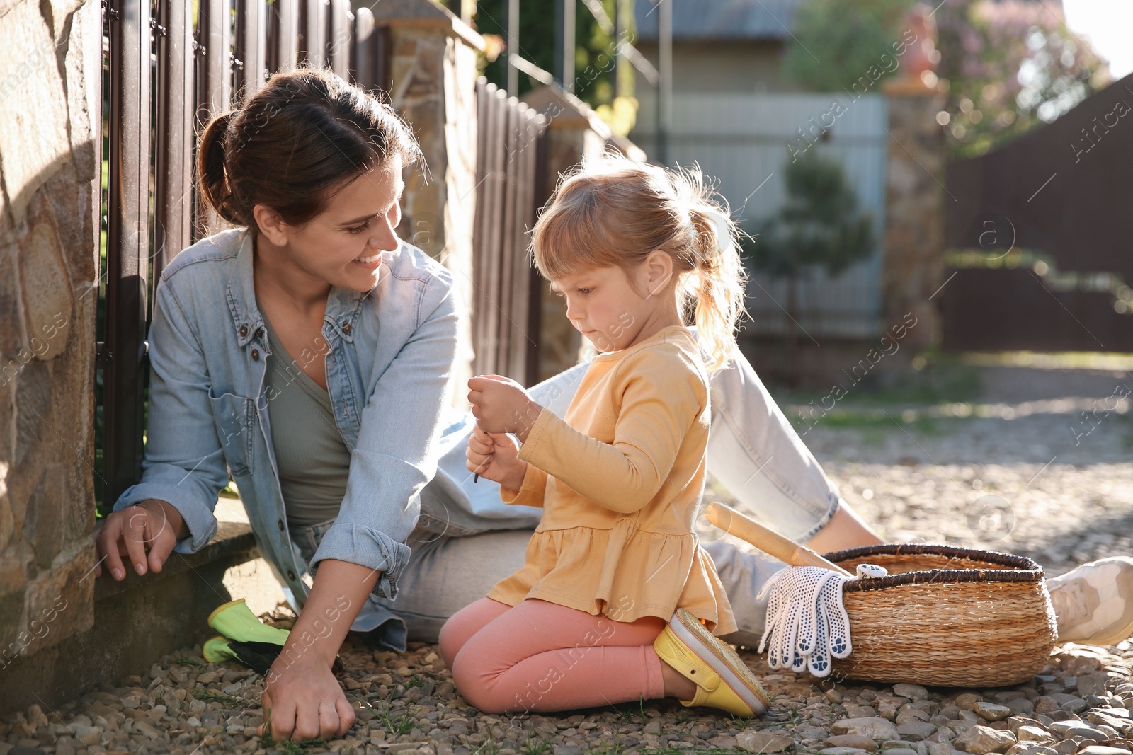 Photo of Mother and her cute daughter spending time together while pulling out grass near house on spring day