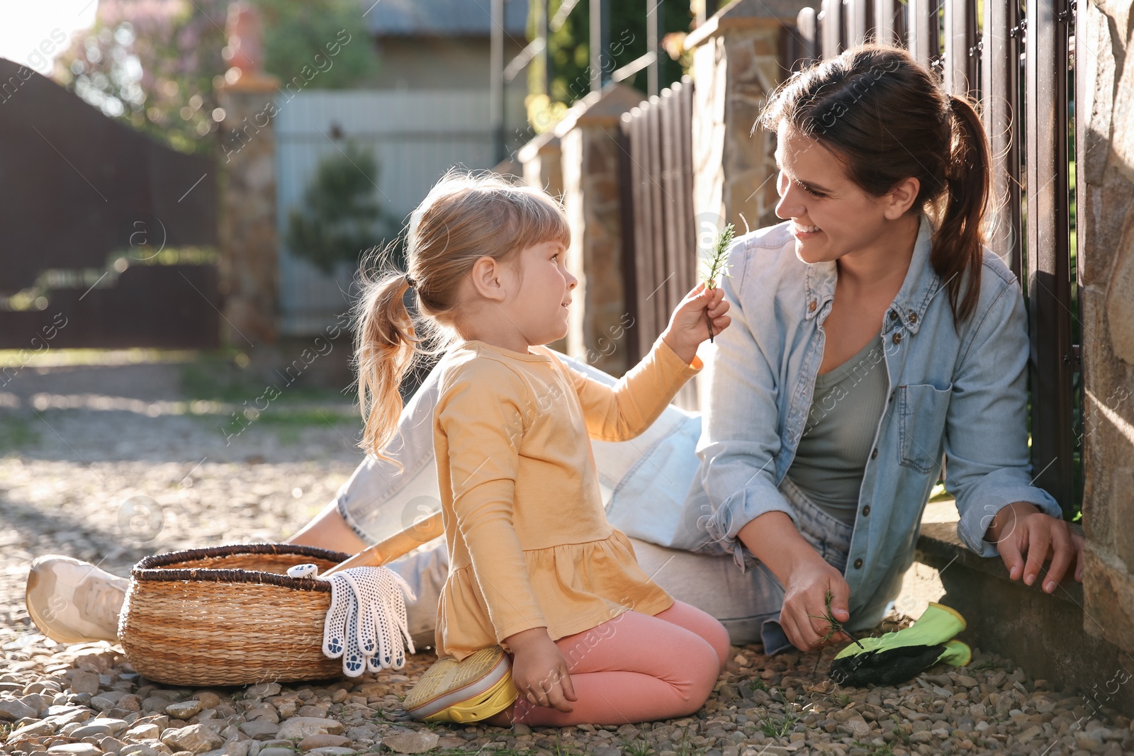 Photo of Mother and her cute daughter spending time together while pulling out grass near house on spring day