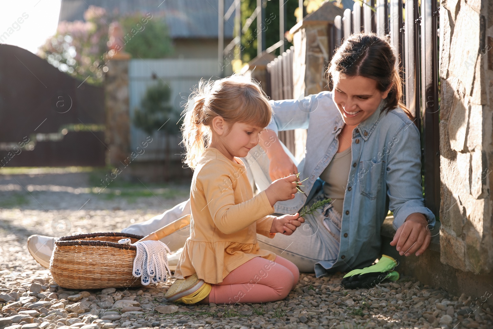 Photo of Mother and her cute daughter spending time together while pulling out grass near house on spring day