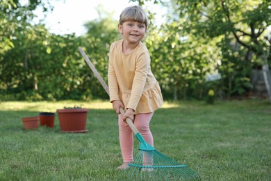 Photo of Cute little girl with rake in garden on spring day