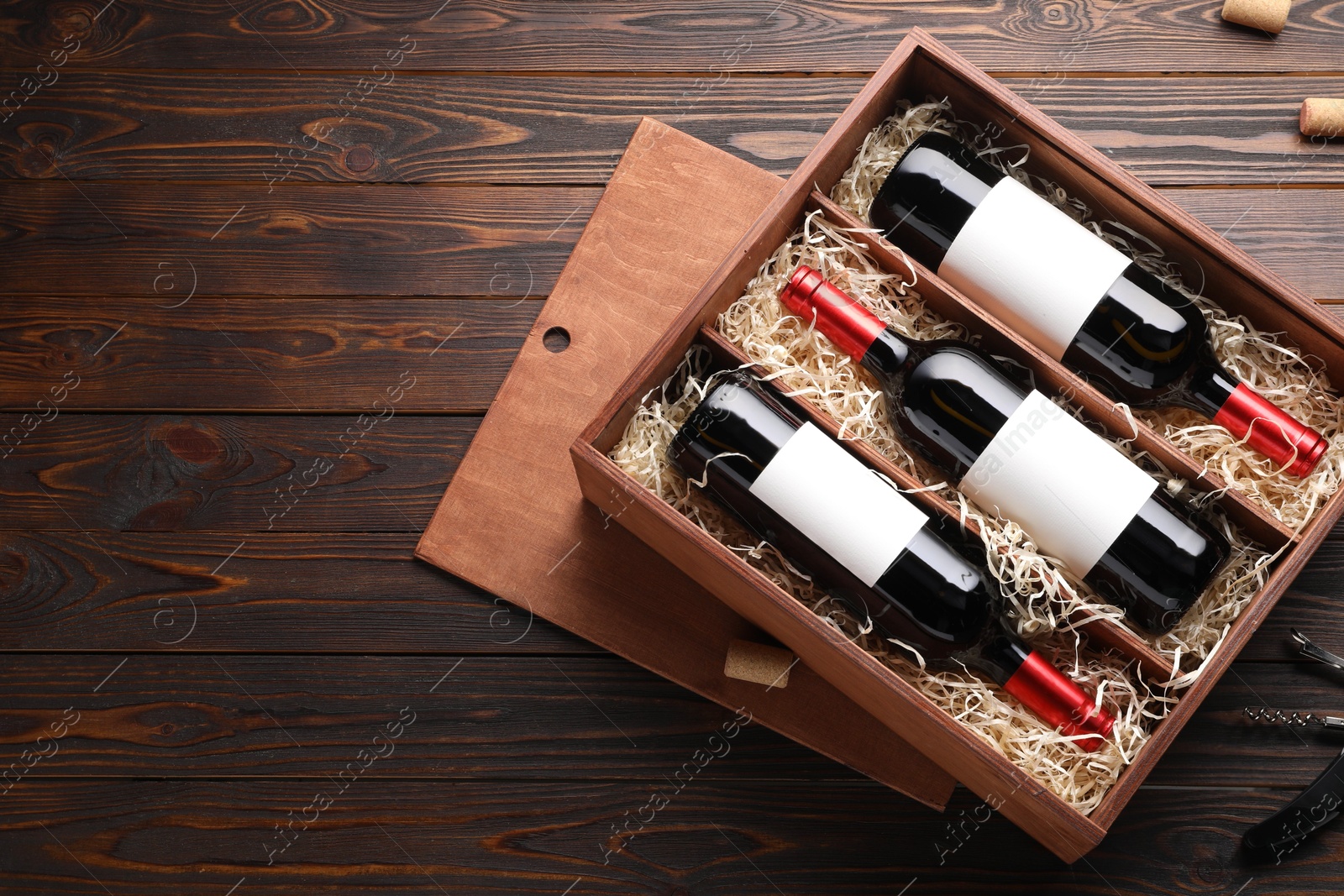 Photo of Box with wine bottles, corkscrew and corks on wooden table, flat lay. Space for text