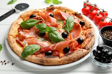 Tasty pizza with cured ham, olives, tomatoes and basil on white wooden table