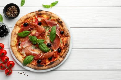 Tasty pizza with cured ham, olives, tomatoes and basil on white wooden table, flat lay. Space for text