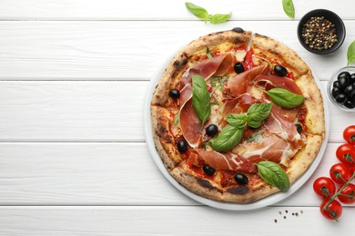 Tasty pizza with cured ham, olives, tomatoes and basil on white wooden table, flat lay. Space for text