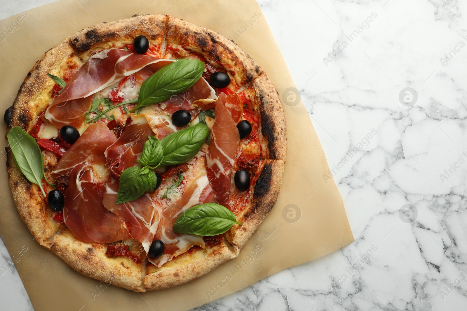 Photo of Tasty pizza with cured ham, olives, sun-dried tomato and basil on white marble table, top view. Space for text