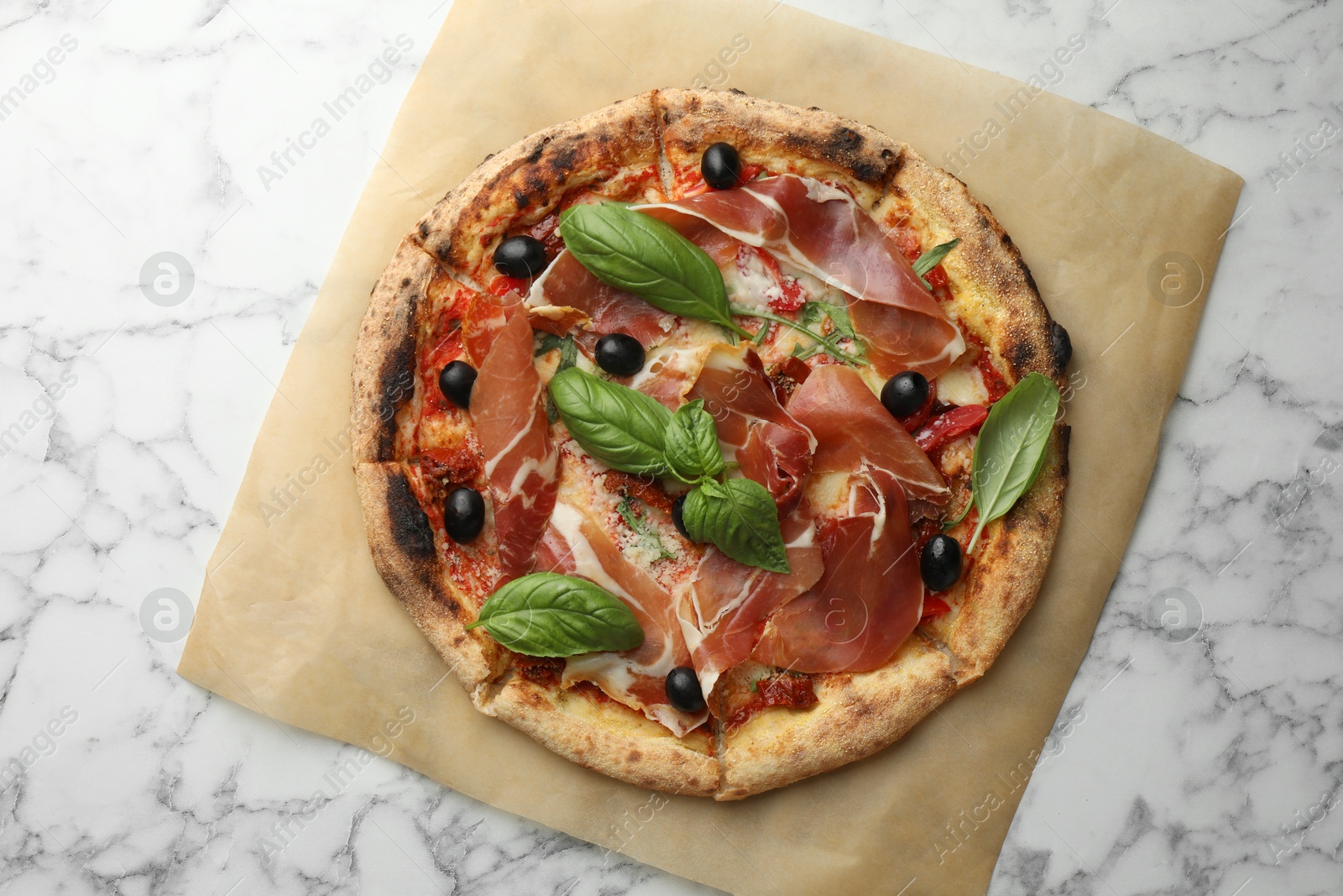 Photo of Tasty pizza with cured ham, olives, sun-dried tomato and basil on white marble table, top view