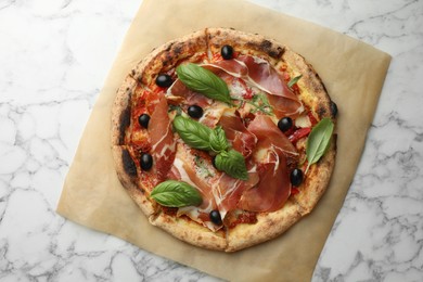 Tasty pizza with cured ham, olives, sun-dried tomato and basil on white marble table, top view