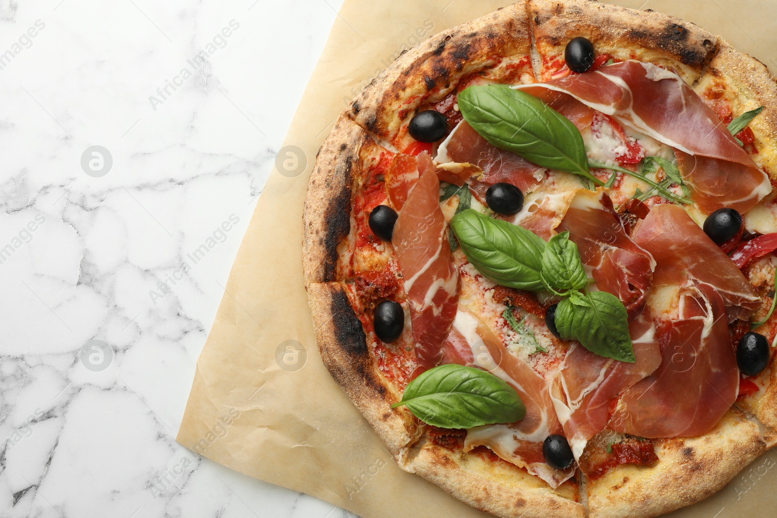 Photo of Tasty pizza with cured ham, olives, sun-dried tomato and basil on white marble table, top view. Space for text