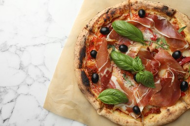 Tasty pizza with cured ham, olives, sun-dried tomato and basil on white marble table, top view. Space for text