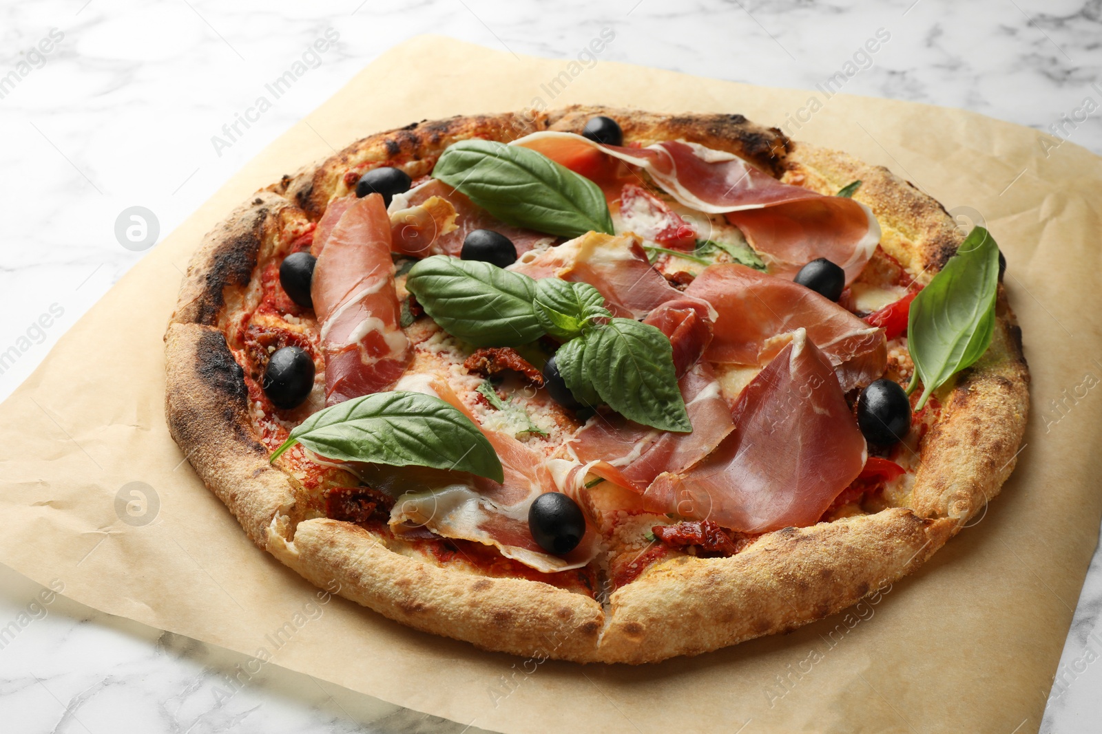 Photo of Tasty pizza with cured ham, olives, sun-dried tomato and basil on white marble table, closeup