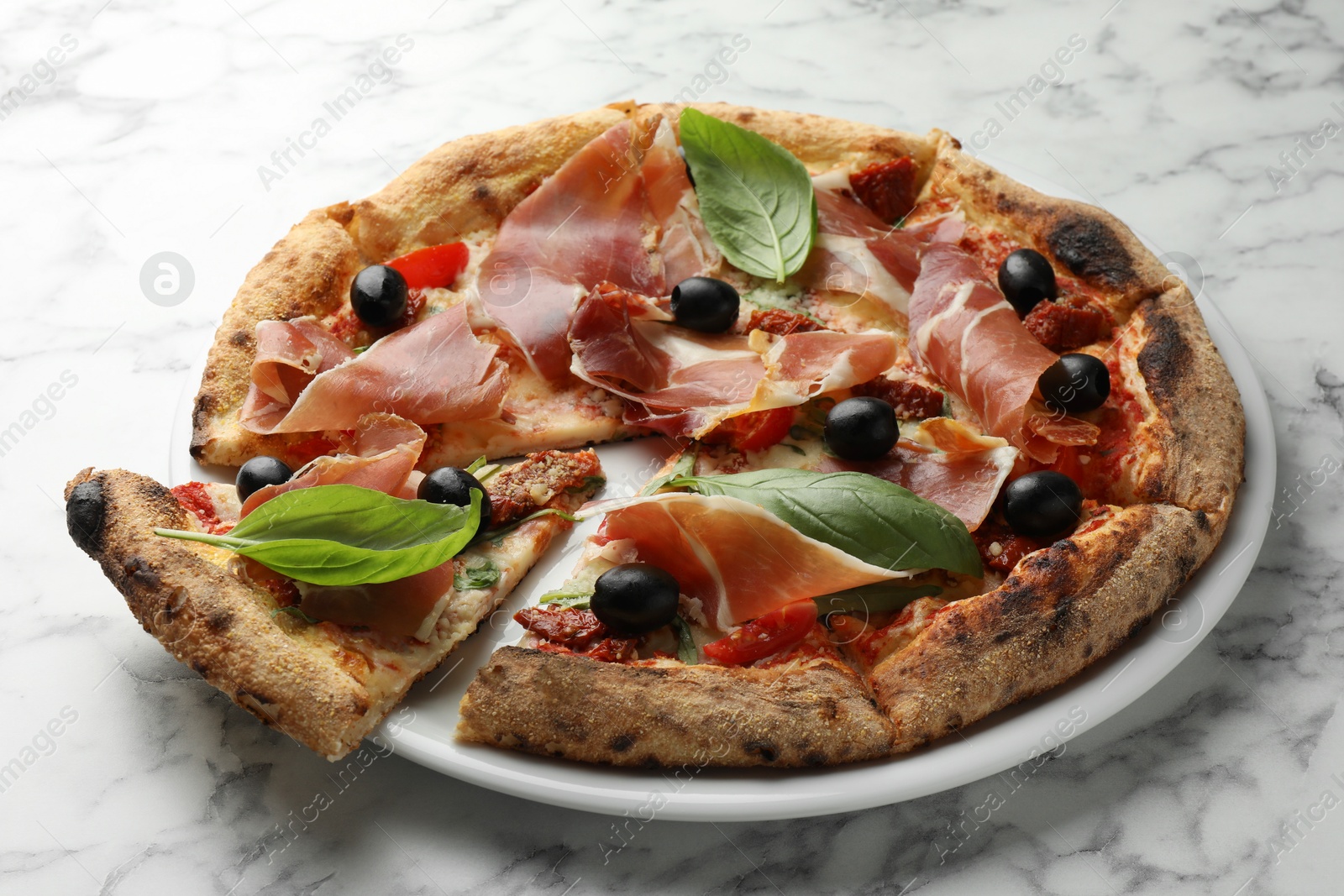 Photo of Tasty pizza with cured ham, olives, sun-dried tomato and basil on white marble table, closeup