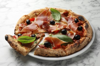 Photo of Tasty pizza with cured ham, olives, sun-dried tomato and basil on white marble table, closeup