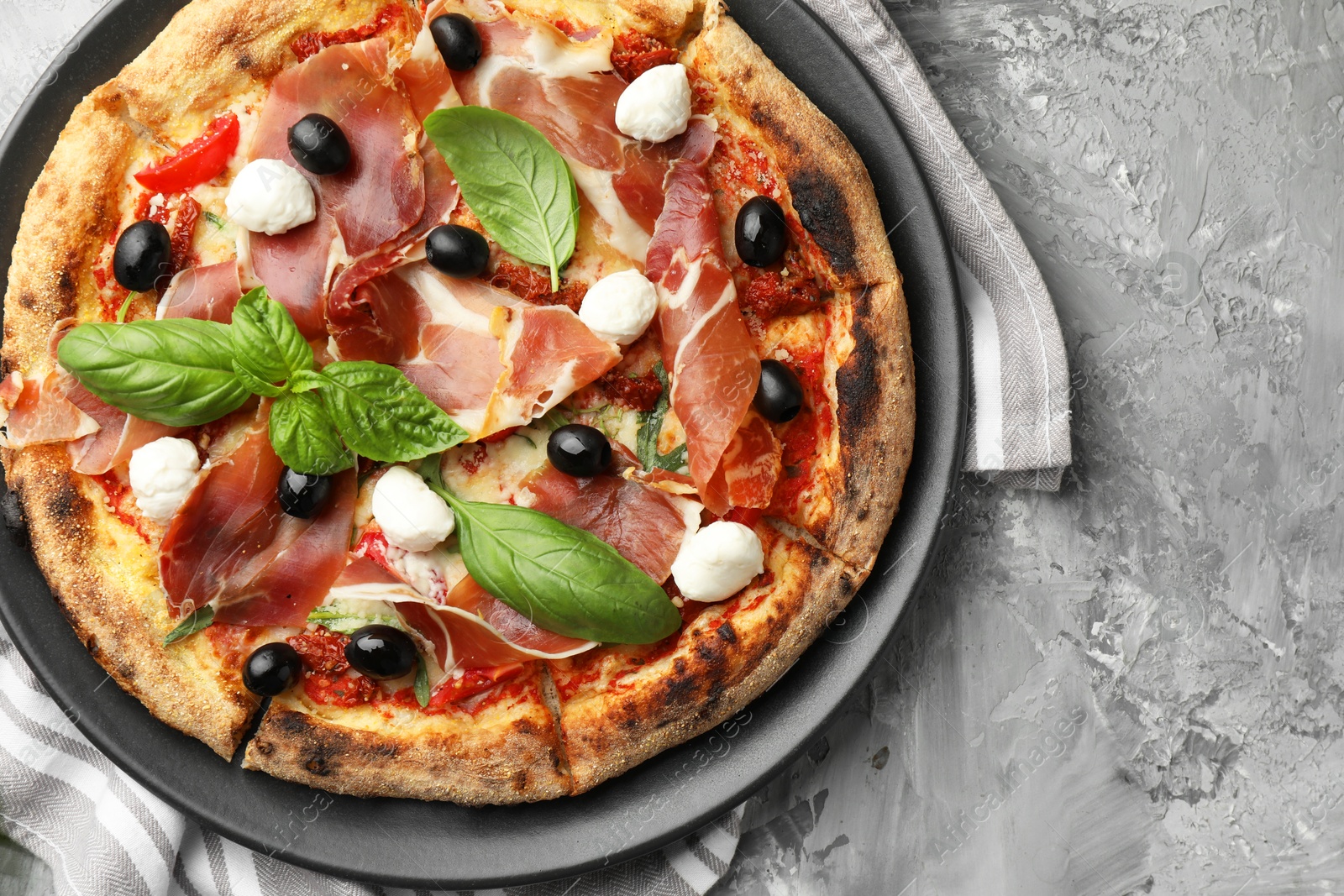 Photo of Tasty pizza with cured ham, olives, mozzarella cheese, sun-dried tomato and basil on gray textured table, top view