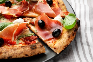 Photo of Tasty pizza with cured ham, olives, mozzarella cheese, sun-dried tomato and basil on table, closeup