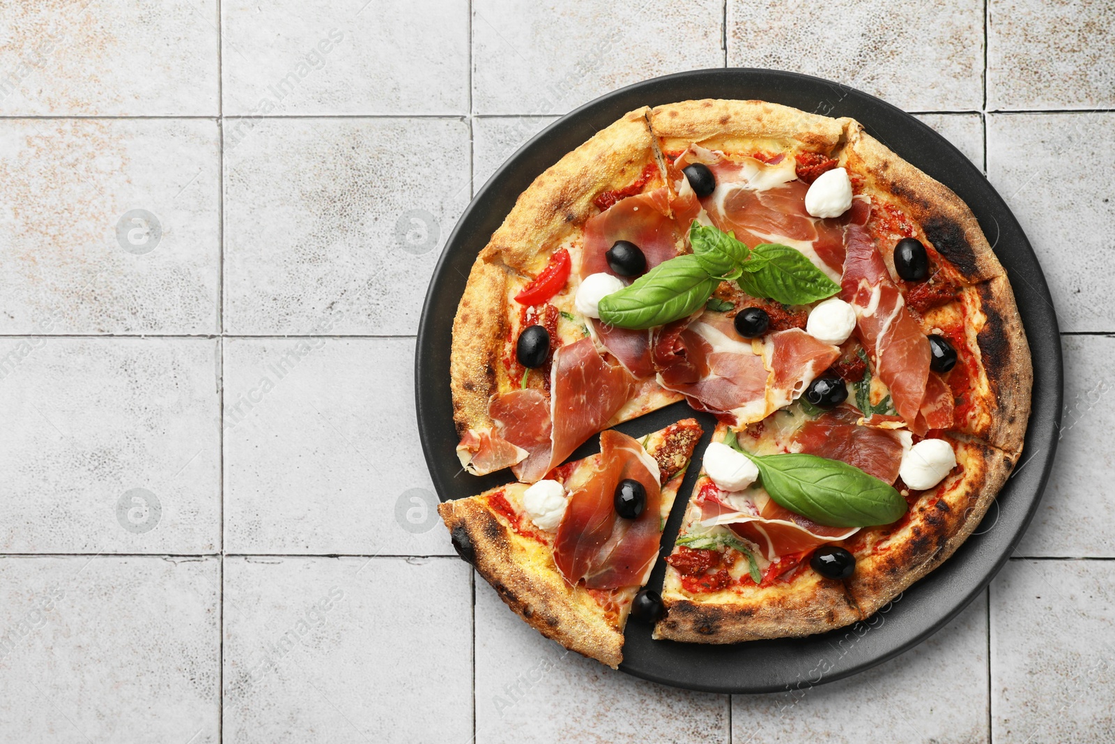 Photo of Tasty pizza with cured ham, olives, mozzarella cheese, sun-dried tomato and basil on light tiled table, top view. Space for text