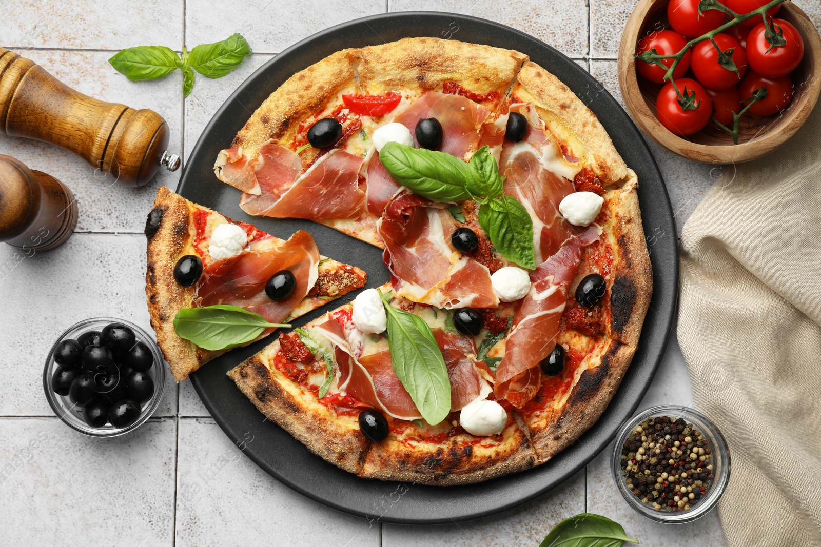 Photo of Tasty pizza with cured ham, olives, mozzarella cheese, tomatoes and basil on light tiled table, flat lay