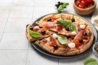 Photo of Tasty pizza with cured ham, olives, mozzarella cheese, tomatoes and basil on light tiled table, closeup